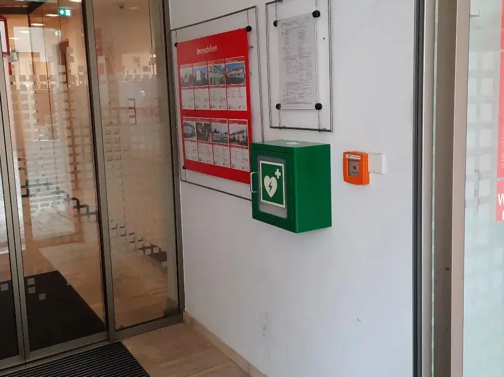 Grüner Defibrillator-Kasten hängt an Wand.