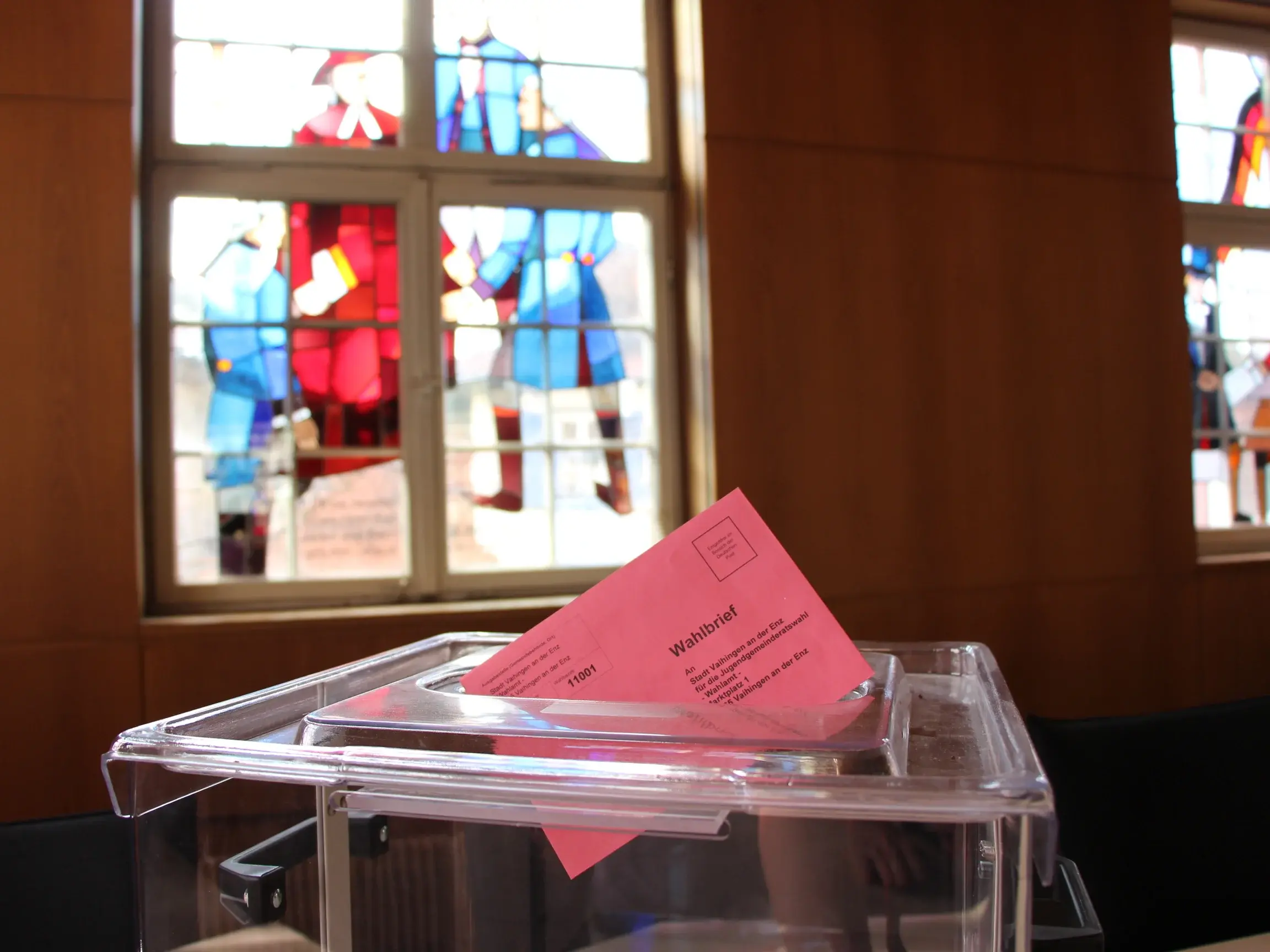Blick auf eine Wahlurne mit Stimmzettel, der im oberen Schlitz steckt